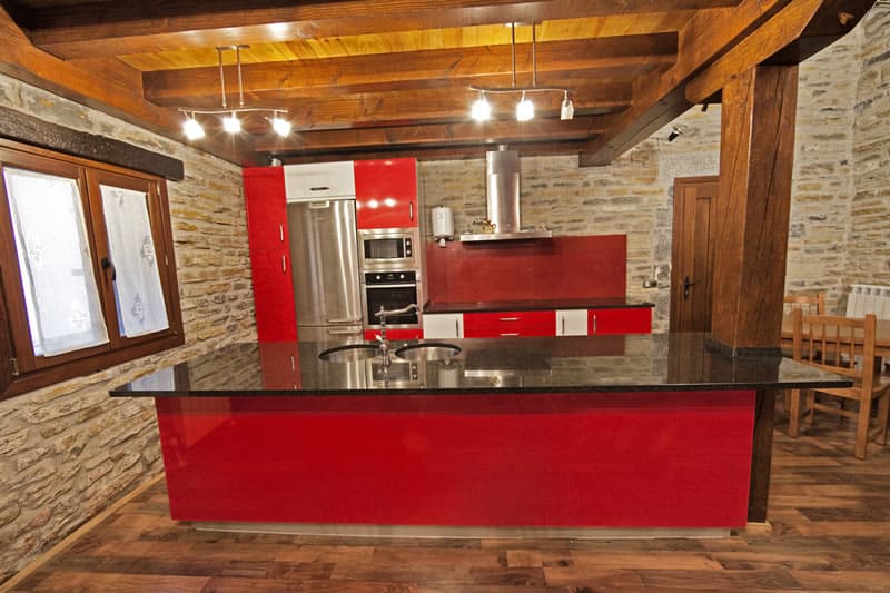 Cocina grande con isla roja y encimera bajo las vigas de madera