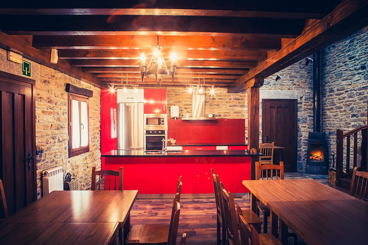Cocina y comedor bajo vigas de madera, con lámpara de araña y mesas corridas