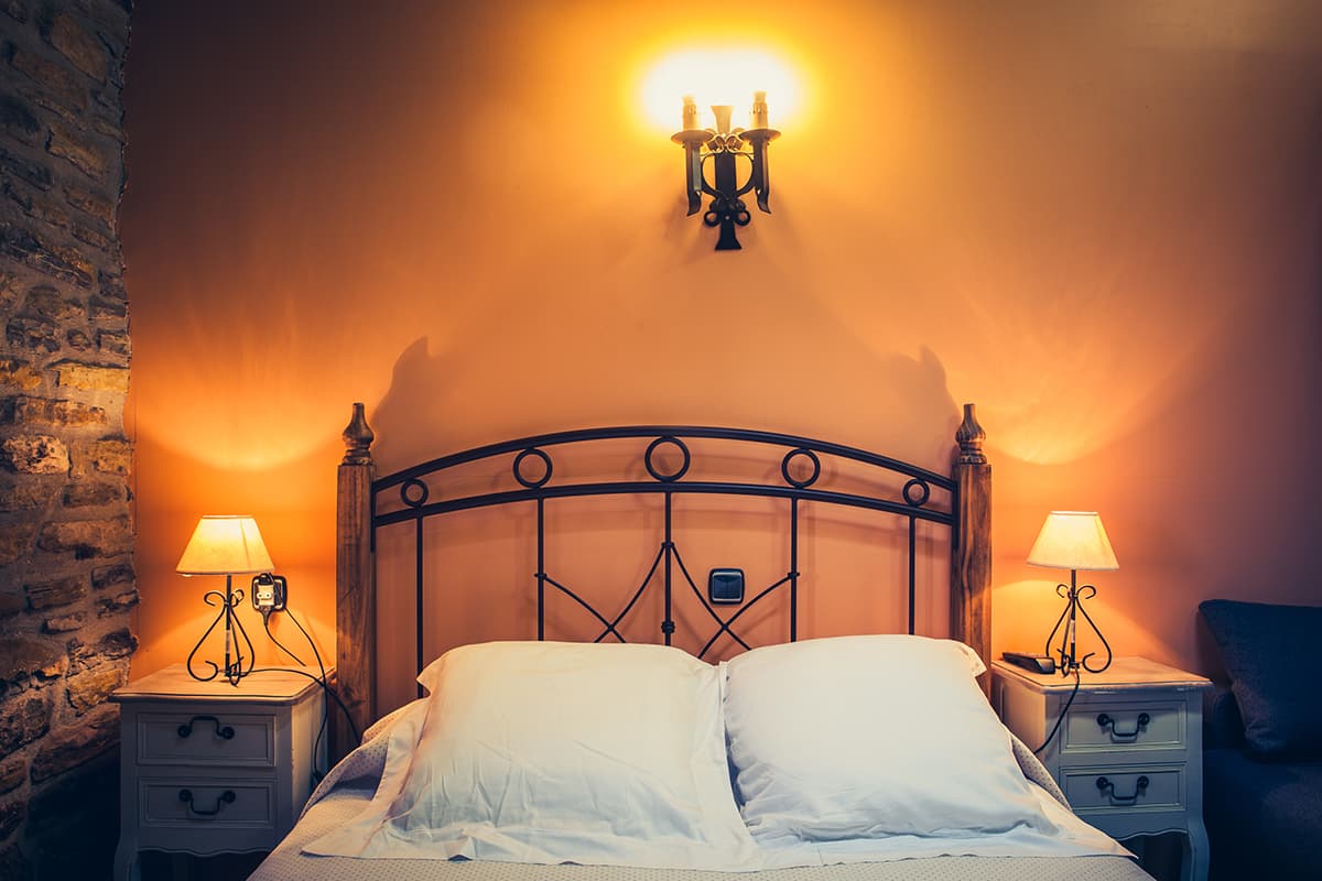 Cama de matrimonio con cabecero de forja entre dos mesillas con lámpara