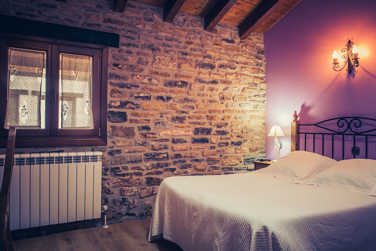 Dormitorio con pared de piedra y ventana de madera junto a la cama