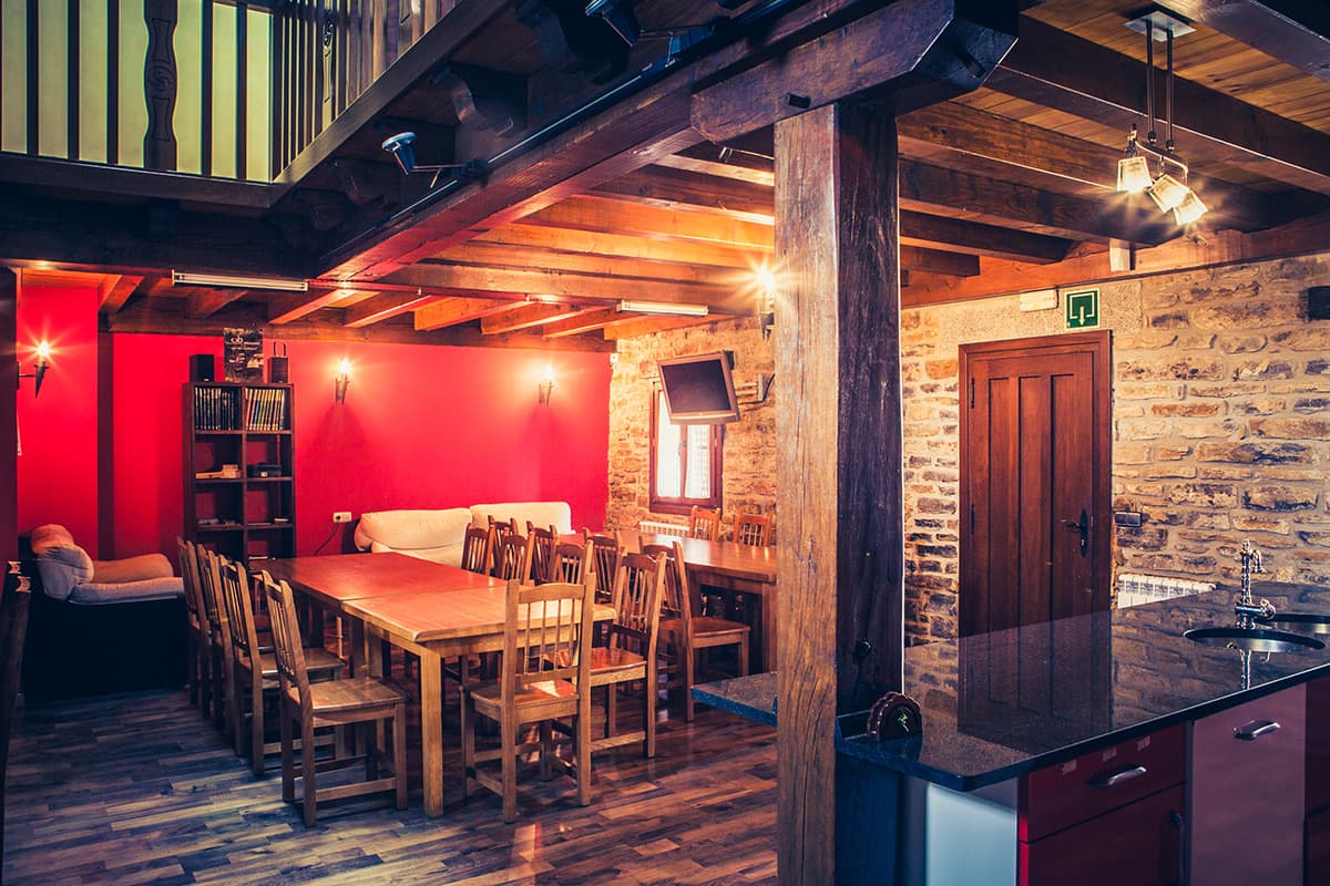 Comedor con vigas de madera, pared roja y mesa larga junto a la cocina