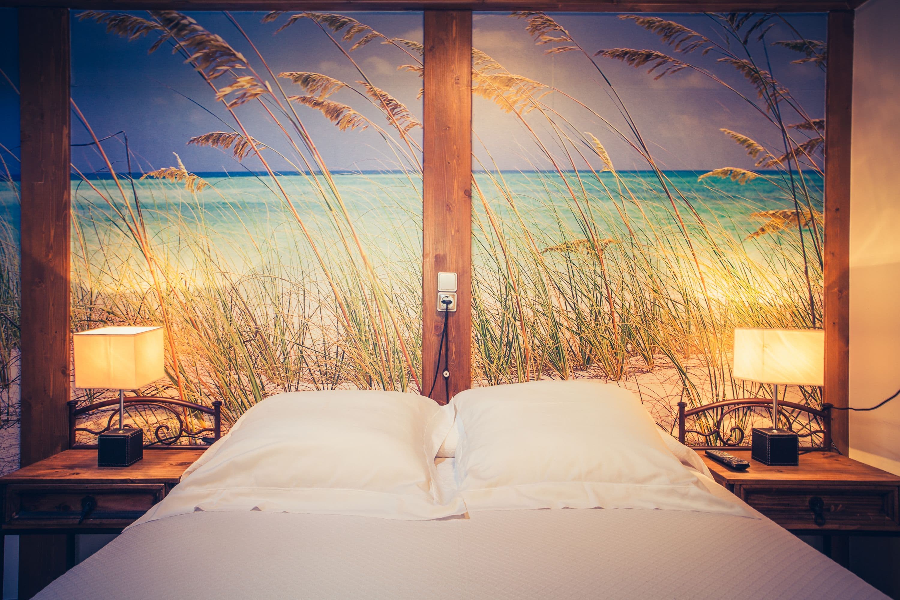 Dormitorio con un mural de dunas y playa detrás del cabecero