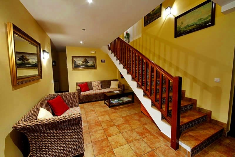 Salón con escalera de madera, sofás y cuadros sobre suelo de barro