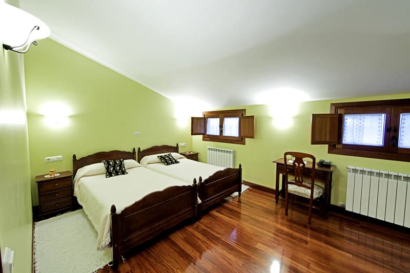 Habitación con cama de matrimonio, suelo de madera y ventanas a dos lados
