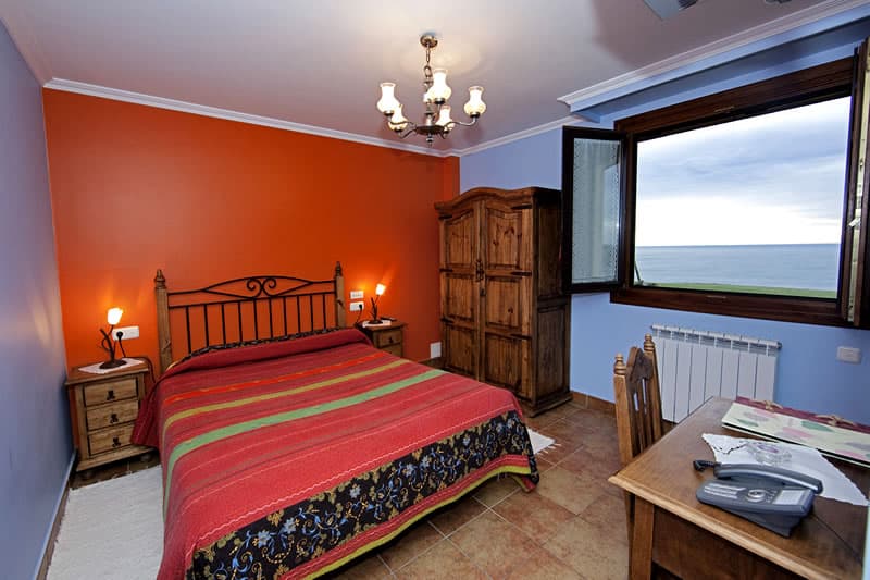 Habitación de pared roja con cama de madera y vistas al mar