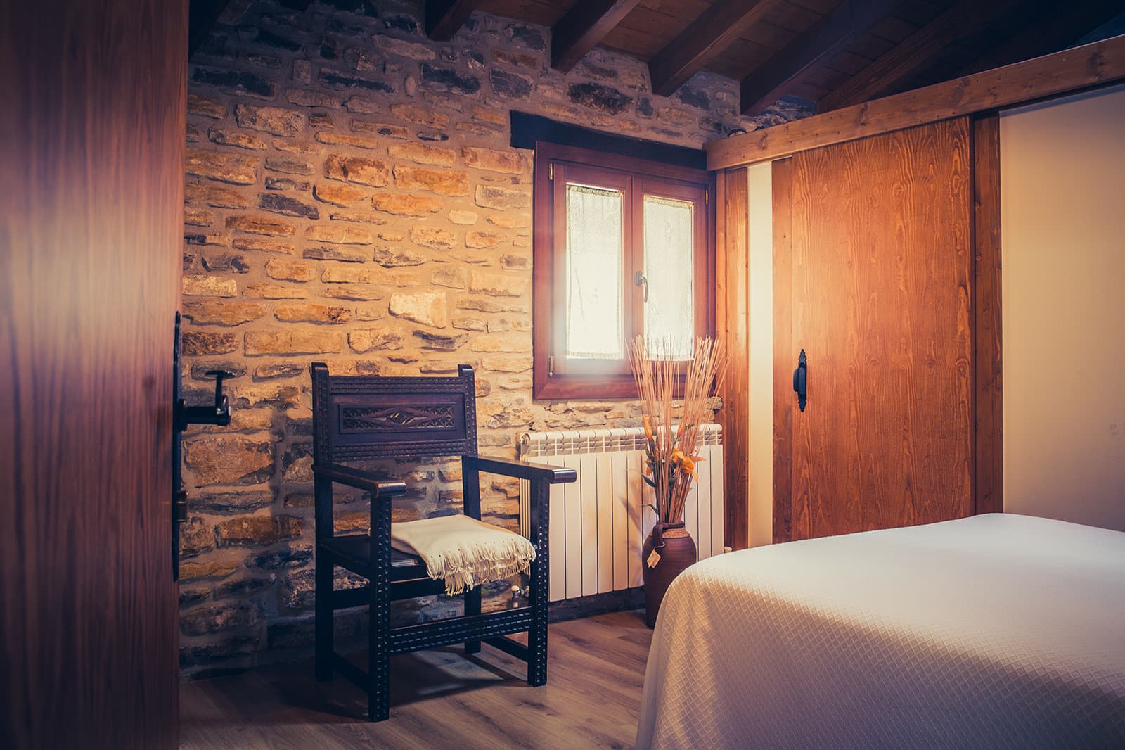 Habitación con pared de piedra vista, ventana de madera y cama de matrimonio