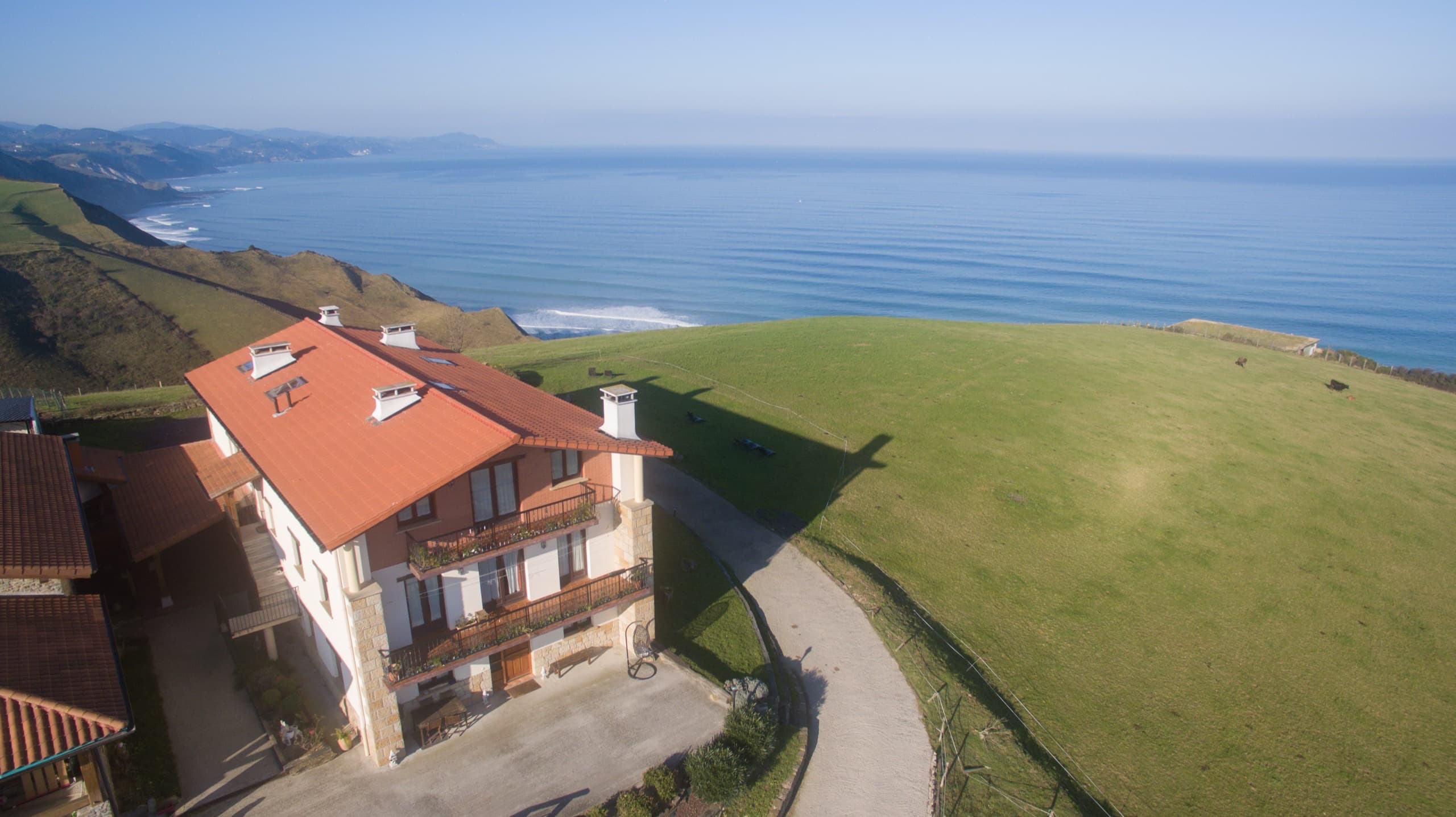 Vista aérea del caserío entre prados, sobre los acantilados del mar