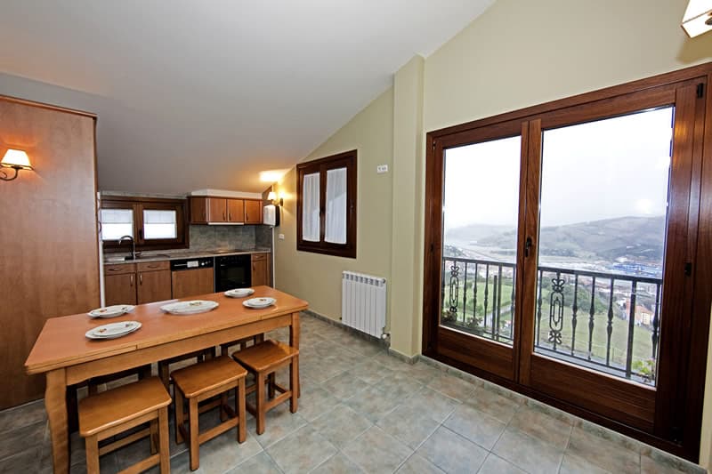 Cocina y comedor del apartamento con mesa de madera junto al ventanal