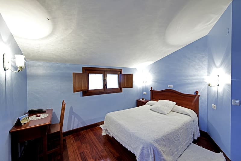 Dormitorio de paredes azul claro con cama de matrimonio y escritorio de madera