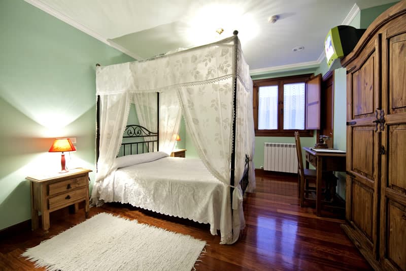Cama con dosel de encaje blanco en una habitación de paredes verde menta